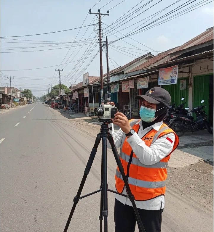 Petugas survei menggunakan alat ukur di tepi jalan untuk pengumpulan data lapangan